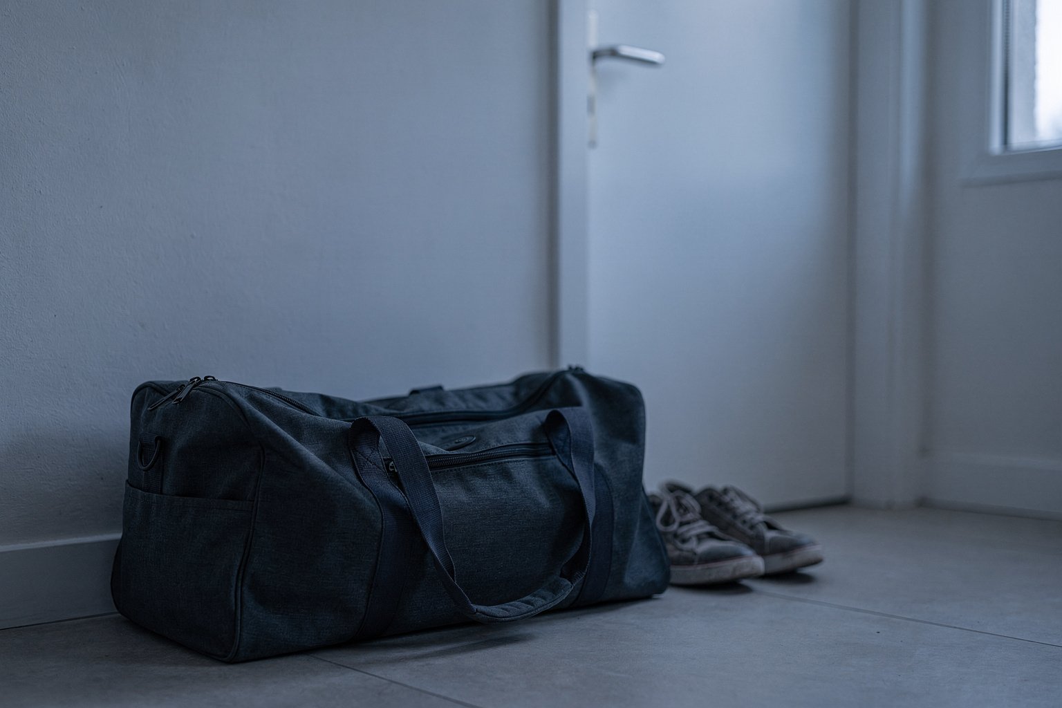 Un sac de natation préparé, posé au sol près d’une porte d’entrée, des chaussures rangées à côté.