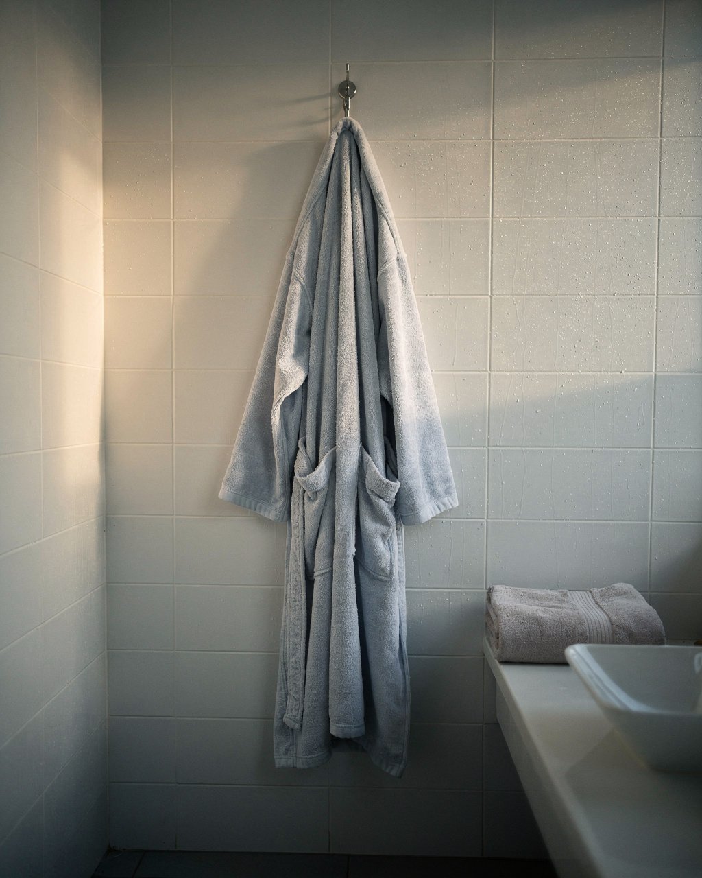 Un peignoir suspendu à un crochet dans une salle de bain, la vapeur encore posée sur le carrelage.